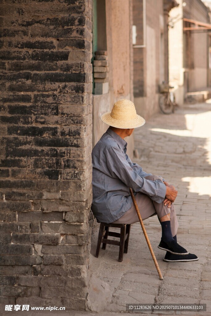 老人坐于古巷墙边休憩