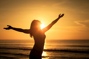 海边女子迎日落舒展双臂