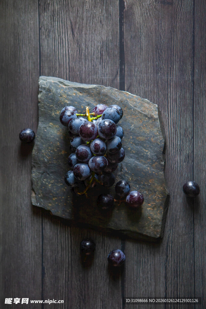 石板上的紫葡萄与散落果粒
