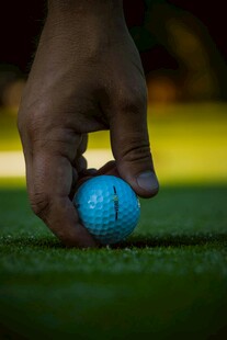 手握蓝色高尔夫球于草地