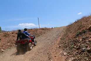 两人驾驶四轮车行驶在土路上