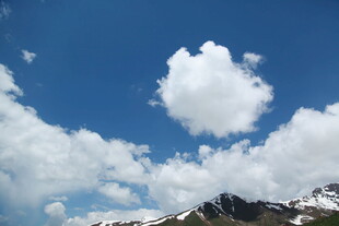 蓝天雪山间的蓬松云朵