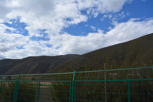 蓝天白云下的山间绿围栏